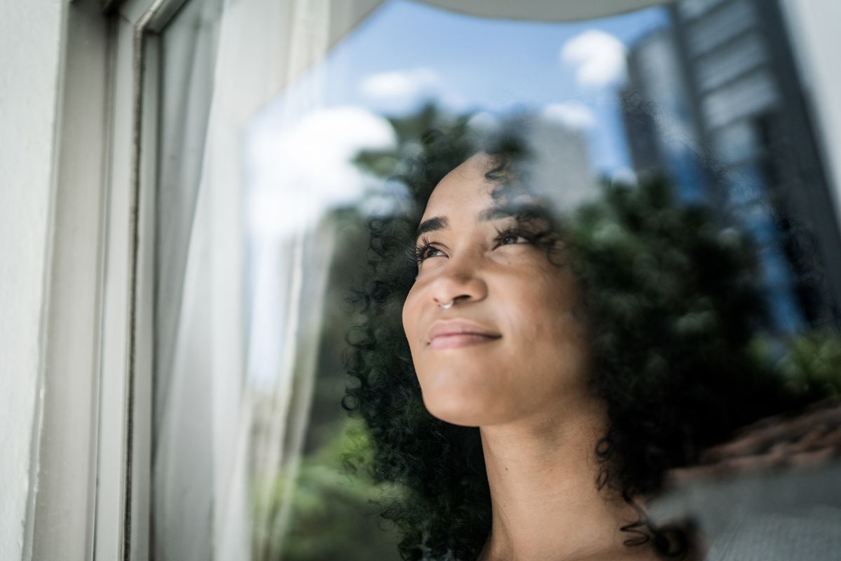 Young woman looking through window at home FG Trade/ iStock